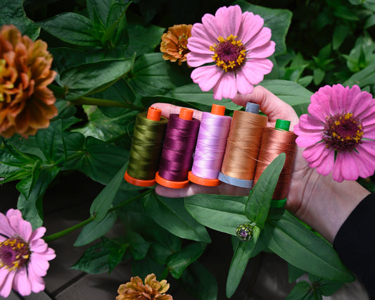Hand is holding 5 spools of thread and held in a bunch of zinnias. 