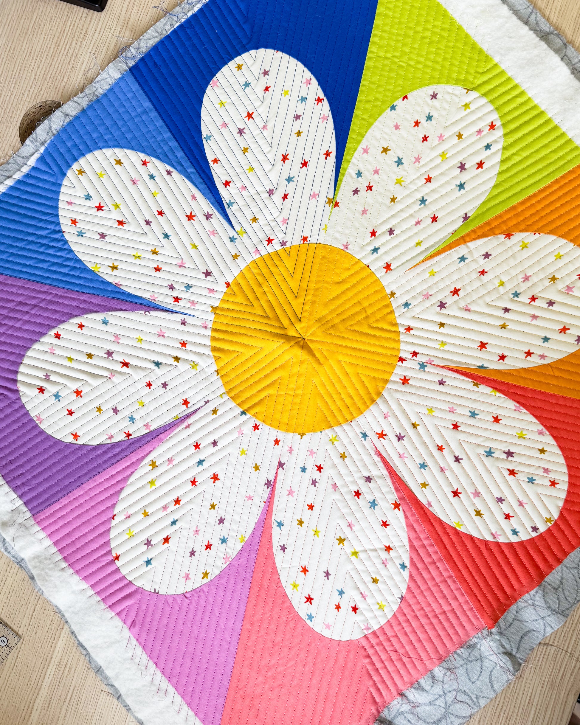 Daisy block with yellow center, cream petals with rainbow starry print, and a rainbow background. 